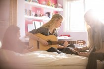 Дівчата-підлітки грають на гітарі і використовують цифровий планшет на ліжку — стокове фото