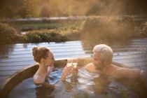 Couple toasting champagne glasses soaking in hot tub on autumn patio — Stock Photo