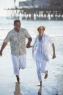Улыбающаяся пожилая пара бегает по солнечному пляжу — стоковое фото