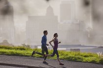 Runner couple running on sunny urban city sidewalk — Stock Photo