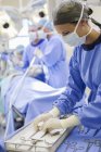 Krankenschwester steht mit Operationswerkzeug am Tablett im Operationssaal — Stockfoto