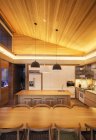 Teto de madeira inclinada iluminada sobre cozinha de luxo e mesa de jantar — Fotografia de Stock
