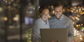 Усміхнений бізнесмен і бізнес-леді працюють пізно в ноутбуці вночі — стокове фото