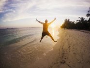 Retrato de homem exuberante pulando na praia tropical ao pôr do sol — Fotografia de Stock