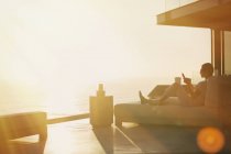 Silhouette femme utilisant téléphone cellulaire sur chaise longue sur balcon de luxe avec vue sur l'océan coucher de soleil — Photo de stock