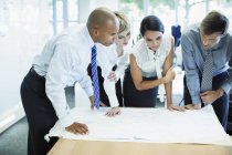 Business people examining blueprints in office — Stock Photo