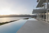 Сонячний, спокійний сучасний розкішний будинок вітрина екстер'єр з нескінченним басейном і видом на океан захід сонця — стокове фото