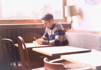 Mann textet mit Handy am Tisch in sonnigem Café-Fenster — Stockfoto