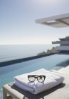 Солнечные очки на сложенном полотенце у бассейна в солнечном роскошном патио с видом на океан — стоковое фото