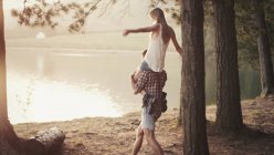 Молодий чоловік носить жінку на плечах на березі озера — стокове фото