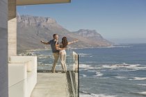 Carefree couple standing on sunny luxury balcony with ocean and mountain view — Stock Photo