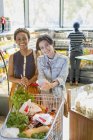 Retrato joven pareja lesbiana con carrito de compras en el mercado de comestibles - foto de stock