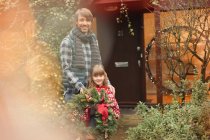 Portrait smiling father and daughter holding Christmas wreath outside house — Stock Photo