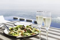 Prato de salada e copos de champanhe na mesa ao ar livre — Fotografia de Stock