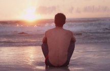 Молодий чоловік на пляжі дивиться захід сонця над океаном — стокове фото