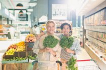 Porträt lächelnde junge Freundinnen mit Grünkohl im Supermarkt — Stockfoto