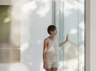 Mulher pensativa em pé na janela ensolarada — Fotografia de Stock