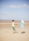 Vento puxando guarda-chuva nas mãos do menino na praia ensolarada de verão — Fotografia de Stock