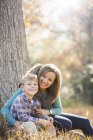 Portrait smiling mother and son at tree trunk in autumn woods — Stock Photo