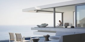 Жінка сидить на сучасному, розкішному будинку вітрина зовнішнього дворика з видом на океан — стокове фото