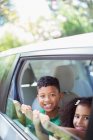 Portrait of happy brother and sister leaning out car window — Stock Photo