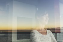 Женщина с видом на закат и океан из окна — стоковое фото