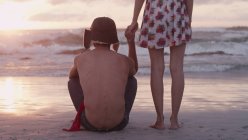Молодая пара, держащаяся за руки на пляже на закате — стоковое фото