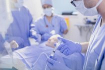 Anesthésiste avec seringue injectant l'anesthésie dans le goutte-à-goutte IV dans la salle d'opération — Photo de stock
