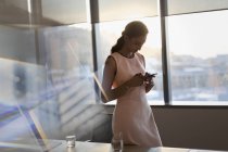 Businesswoman texting with cell phone in sunny conference room — Stock Photo