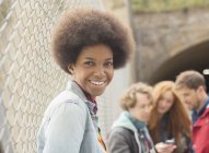 Woman smiling by chain link fence with friends in background — Stock Photo