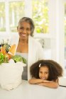 Portrait de sourire de grand-mère et sa petite-fille avec épicerie dans cuisine — Photo de stock