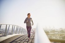 Corridore femminile che corre sul ponte pedonale urbano soleggiato all'alba — Foto stock