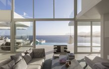 Sunny, tranquila casa de lujo moderna escaparate sala de estar interior con patio y vista al mar - foto de stock