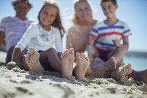 Familia sentada junto con los pies en arena - foto de stock