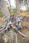 Kinder sitzen auf Baumwurzeln im Wald — Stockfoto