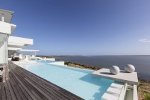 Sunny, tranquila casa de lujo moderna escaparate piscina infinita exterior con vista al mar bajo el cielo azul - foto de stock