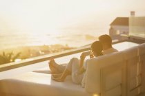 Silhouette Paar mit Handy auf Chaiselongue mit Sonnenuntergang Meerblick — Stockfoto