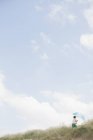 Menino com guarda-chuva listrado andando na grama da praia abaixo do céu azul de verão — Fotografia de Stock