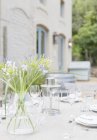 Bouquet on sunny patio table with place settings — Stock Photo