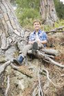 Хлопчик сидить на корінні дерева в лісі — стокове фото