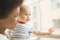 Madre e bambino guardando fuori dalla finestra insieme — Foto stock