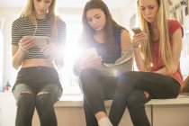 Teenage girls texting with cell phones in kitchen — Stock Photo