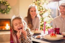 Retrato menina brincalhão em papel coroa soprando favor festa na mesa de jantar de Natal — Fotografia de Stock
