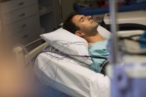 Пацієнт, прикріплений до обладнання медичного моніторингу, лежить у ліжку у відділенні інтенсивної терапії — стокове фото