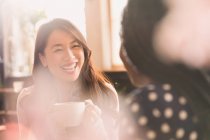 Riendo mujeres hablando y tomando café en la cafetería - foto de stock