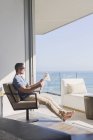 Hombre relajante diario de lectura en la puerta del patio soleado con vista al mar - foto de stock