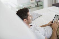 Mann mit digitalem Tablet im Bett — Stockfoto