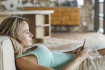 Mujer acostada en el sofá y mensajes de texto con teléfono celular - foto de stock