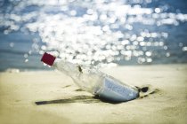 Послание в бутылке на пляже против воды — стоковое фото