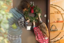 Father and daughter hanging Christmas wreath on front door — Stock Photo